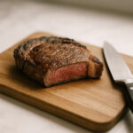 Juicy medium-rare steak resting on a wooden cutting board with a kitchen knife beside it, illustrating meat resting.