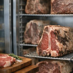 Dry-aged beef steaks on metal racks inside a refrigerated dry aged dolabı meat aging cabinet.