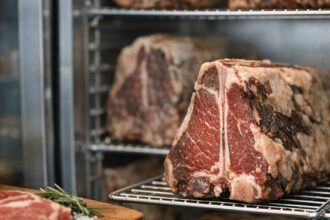 Dry-aged beef steaks on metal racks inside a refrigerated dry aged dolabı meat aging cabinet.