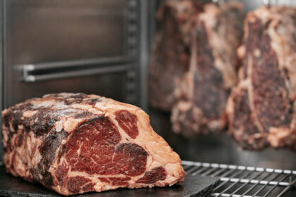 Dry-aged beef steaks on metal racks inside a professional meat curing refrigerator, showcasing the aging process.