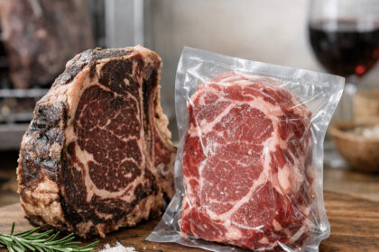 Vakumla paketlenmiş çiğ biftek ile pişmiş antrikot, kesme tahtasında ve yanında kırmızı şarap.