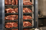 High-quality raw steaks displayed on racks inside a stainless steel steak refrigerator for optimal aging and storage.