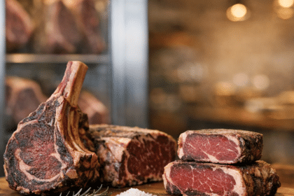 High-quality dry aged ribeye and tomahawk steaks on a wooden board, seasoned and ready for sale.