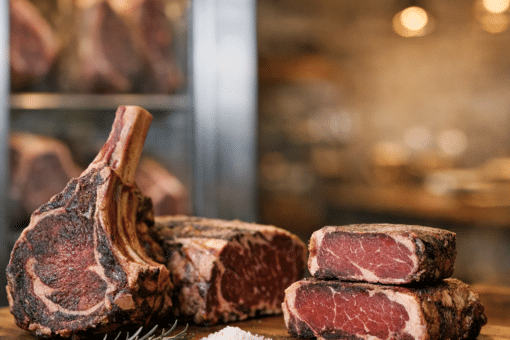 High-quality dry aged ribeye and tomahawk steaks on a wooden board, seasoned and ready for sale.