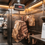 Dry aged dolabında kancada asılı kemikli et parçası ve dijital tartı ile haftalık fire takibi