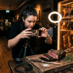 Restoranda dry aged eti telefonla çeken içerik üreticisi, arkada aydınlatmalı dry aged vitrini