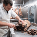 Soğuk odada dry aged et kütüğünün koyu kabuğunu uzun bıçakla tıraşlayan kasap