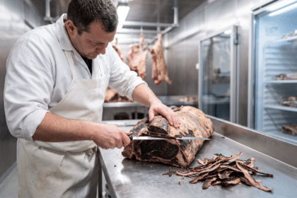 Soğuk odada dry aged et kütüğünün koyu kabuğunu uzun bıçakla tıraşlayan kasap