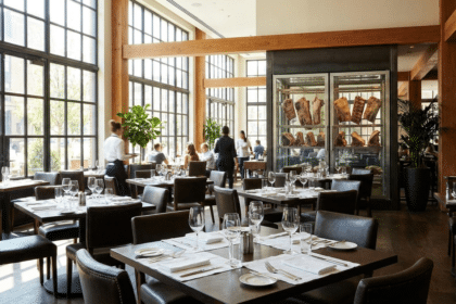 Gün ışığı alan modern steakhouse salonunda öğle servisi ve arka planda dry aged vitrini