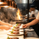 Steakhouse açık mutfağında pass bölümünde tabak hazırlayan şefler ve servisi bekleyen garson