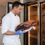 Kasap, dry aged dolabından dinlenmesi tamamlanmış koyu kabuklu bir dana kütüğünü çıkarıyor